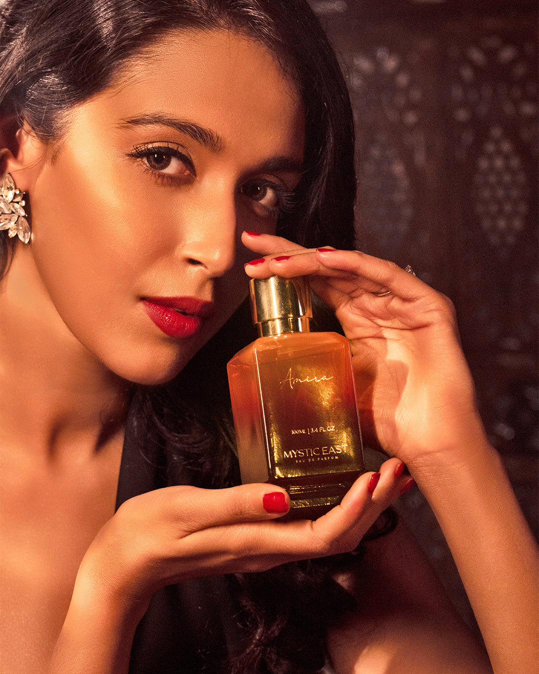 Woman holding a gold bottle of perfume with a dark background