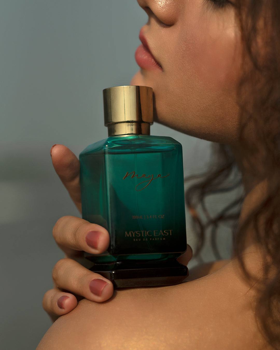 Person holding a teal perfume bottle with gold cap, brand 'Mystic Beast' visible