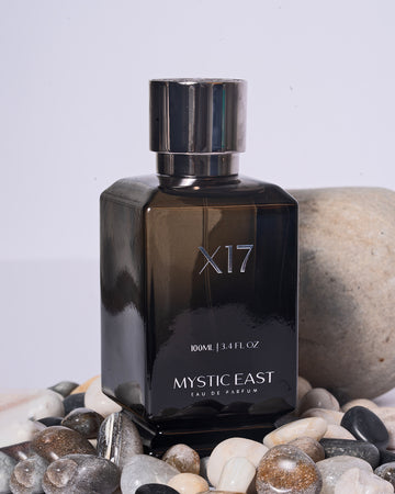 Black perfume bottle labeled 'X17 Mystic East' on a pebble background